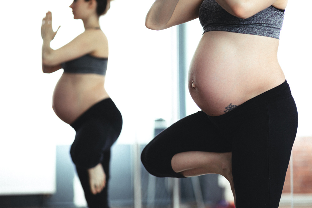 Zwei schwangere Frauen in einer Yoga Pose, Fokus auf dem Babybauch